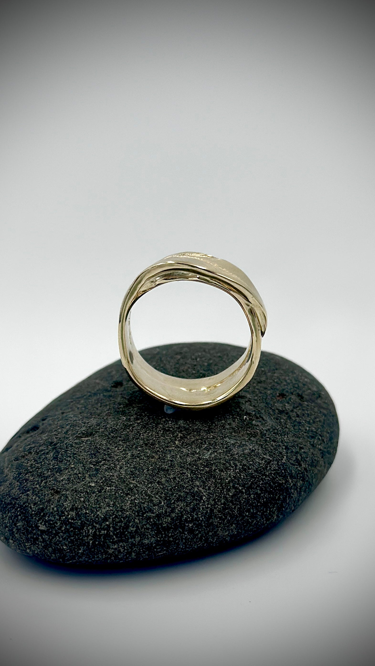 9 carat yellow gold feather ring standing upright on dark river stone, front view showing open band — Marina Fox Fine Art
