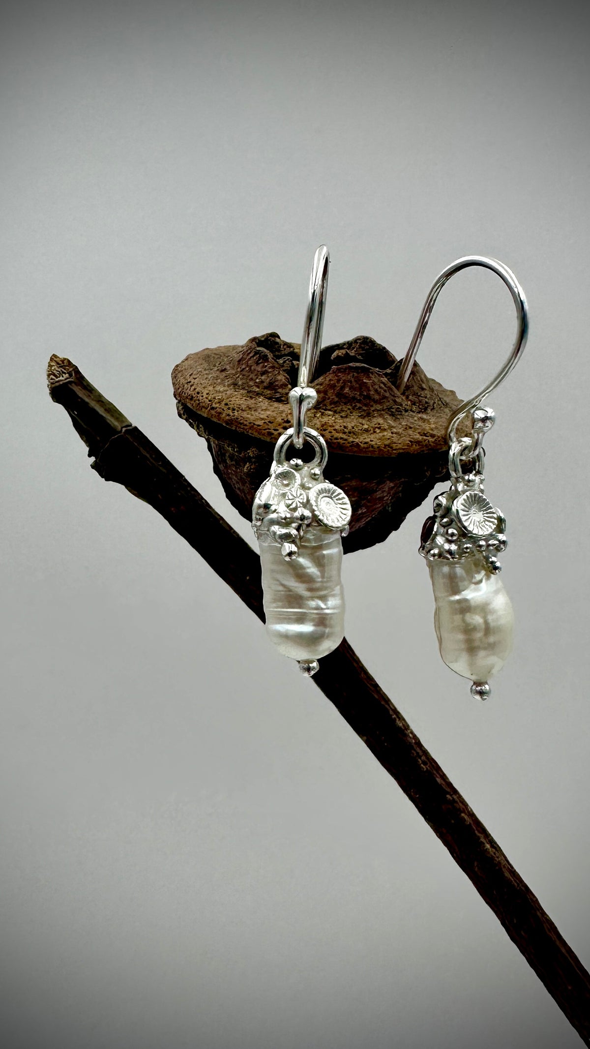 Baroque freshwater pearl drop earrings with sculptural sterling silver coral caps on sterling silver hooks, draped over weathered coastal seed pod