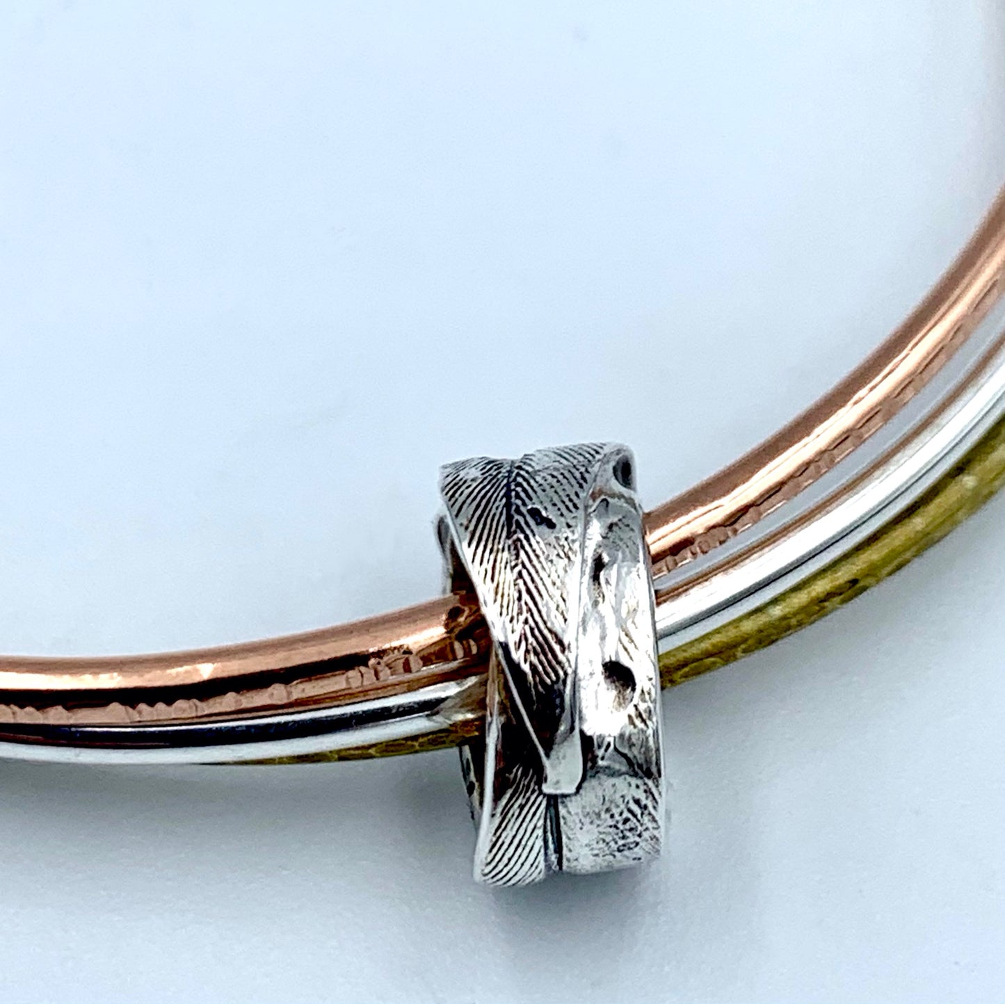 Close-up of one-of-a-kind sterling silver feather bead on triple bangle, lost wax cast from a real feather