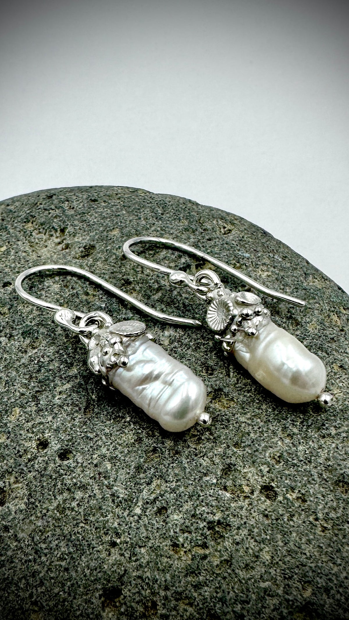 Close-up side view of baroque freshwater pearl drop earrings with hand-formed sterling silver coral cluster caps, resting on granite stone