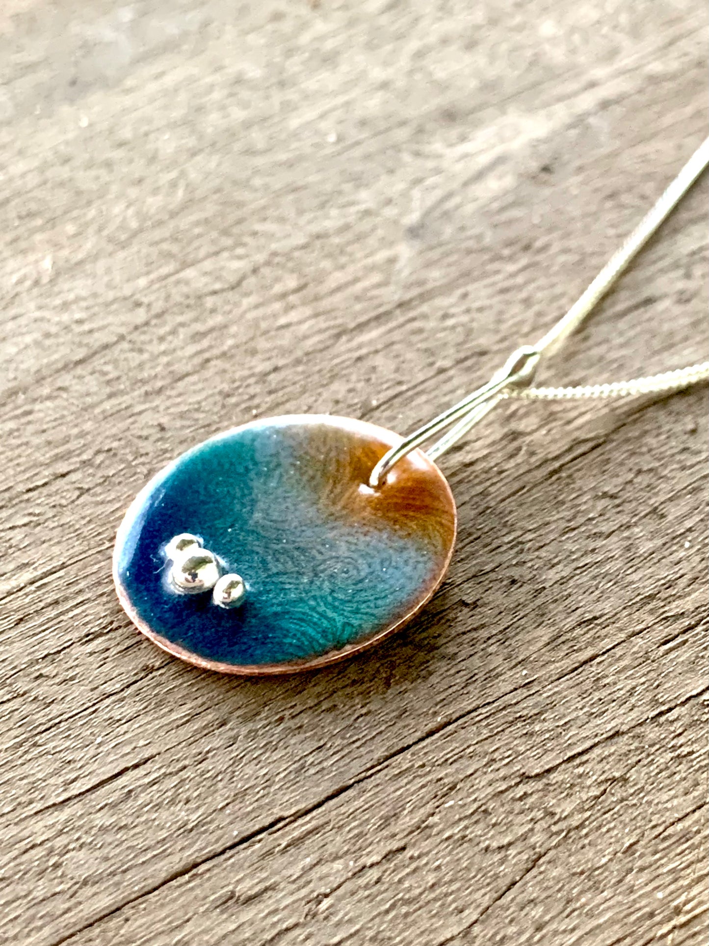 Close-up of copper enamel pendant showing deep blue, purple and clear wave pattern on 25mm disk