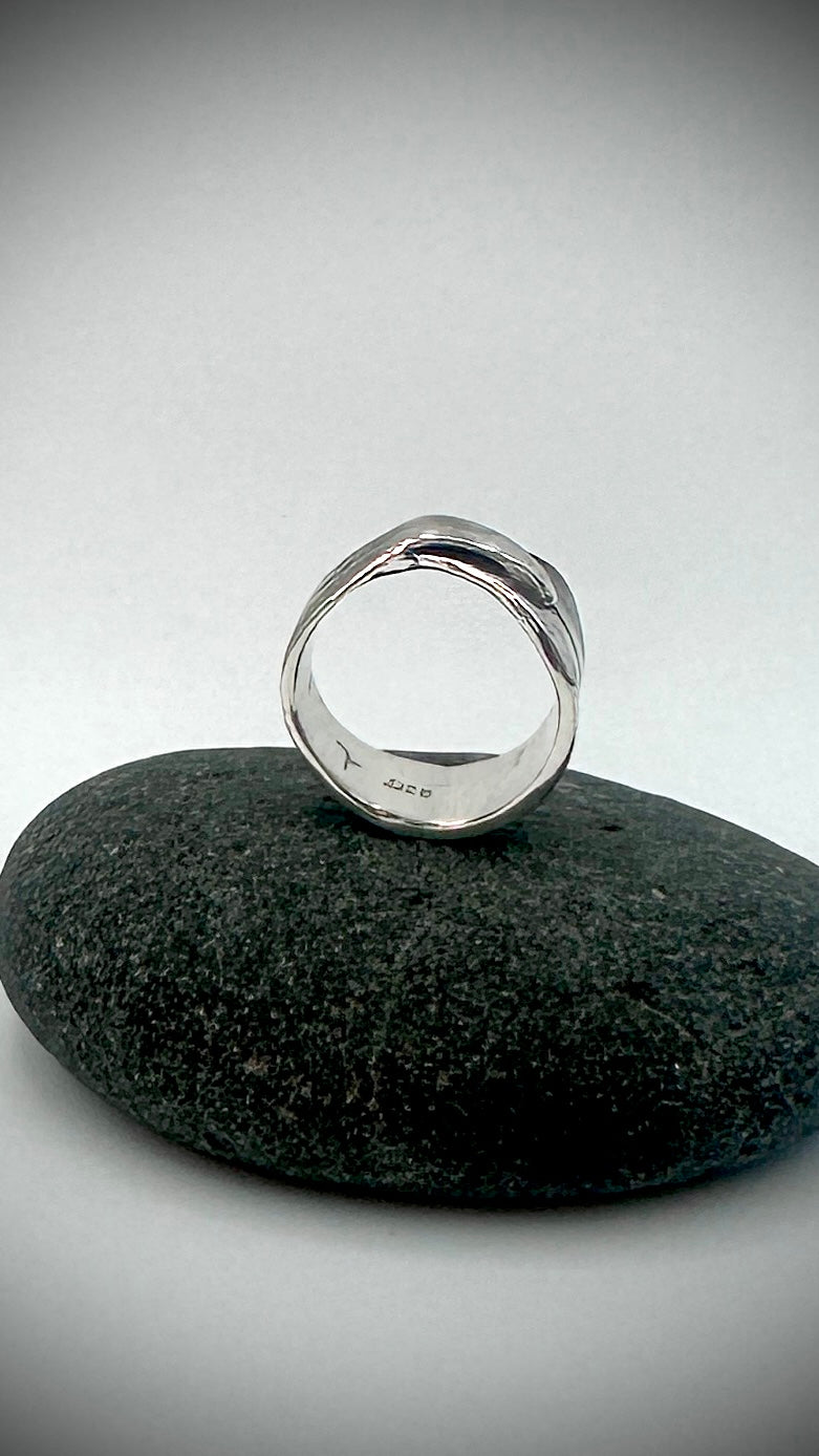 Front view of sterling silver bird's feather ring upright on dark river stone, displaying open band form with smooth polished interior and .925 hallmark — Marina Fox Fine Art