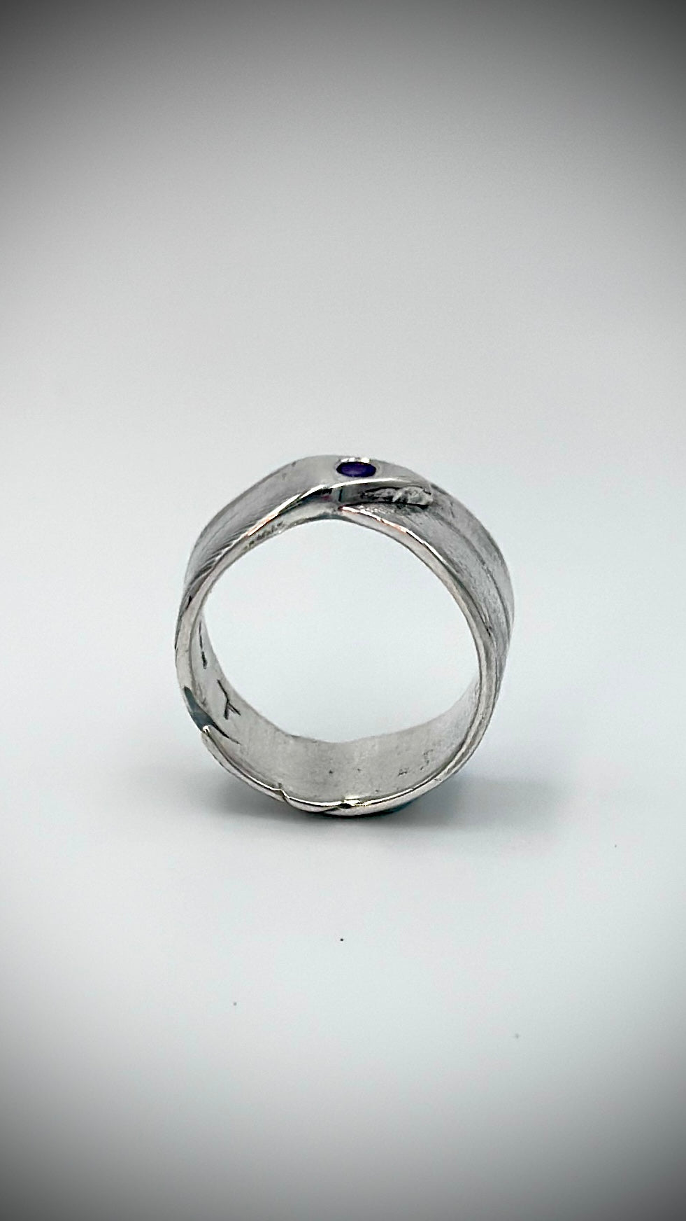 Front view of sterling silver feather ring with flush-set amethyst gemstone, showing wide open band and fine lost wax cast feather barb detail — Marina Fox Fine Art