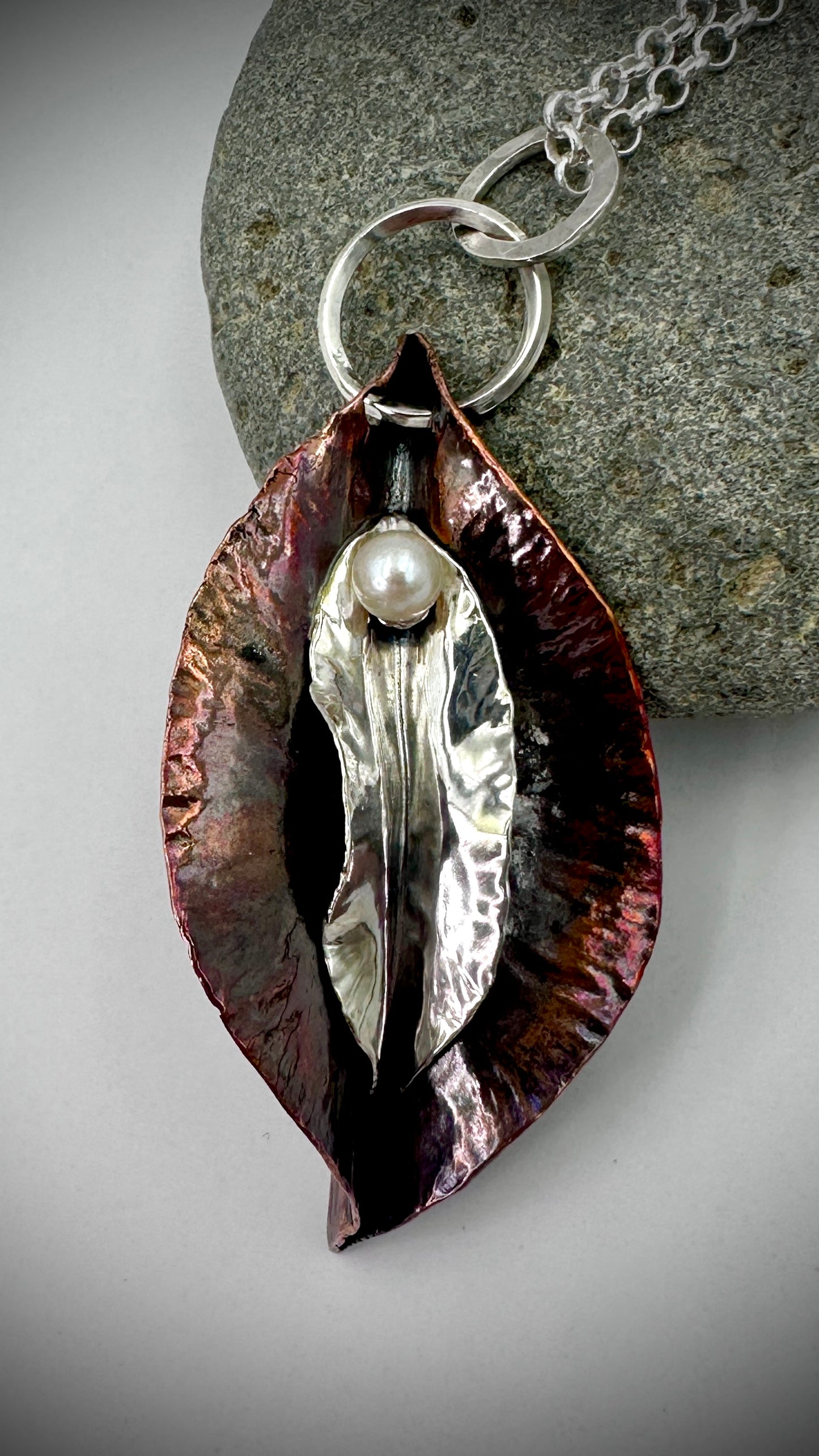 Portal - hammered copper and sterling silver pendant with freshwater pearl, displayed on grey river stone against white background