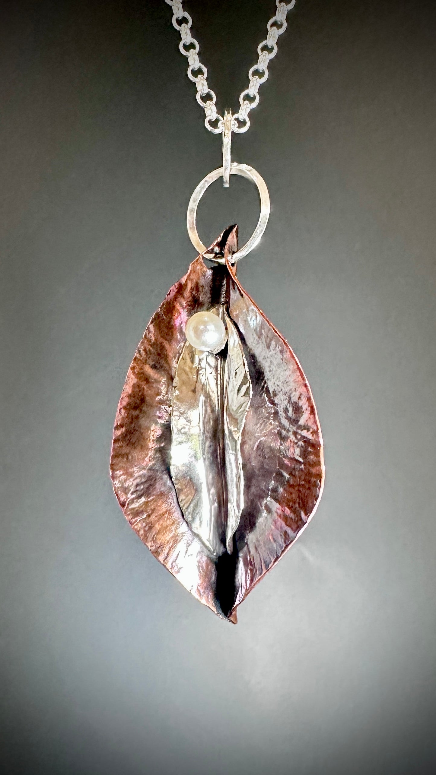 Hammered copper and sterling silver yoni pendant with freshwater pearl suspended on sterling silver belcher chain against grey background