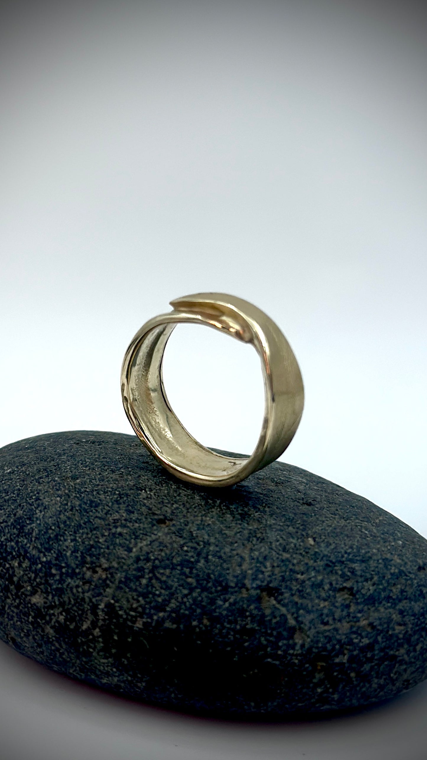 Handcrafted 9 carat gold feather ring standing upright on dark river stone, showing delicate lost wax cast feather texture — Marina Fox Fine Art