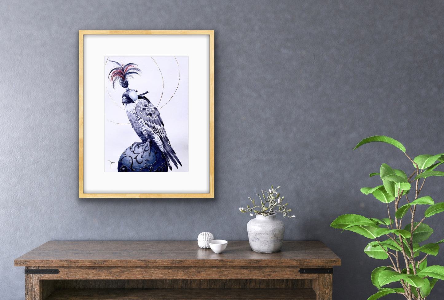 'Medieval Falcon' Peregrine Falcon fine art print by Marina Fox, framed in natural timber, displayed above a rustic oak console with a white ceramic vase and botanicals against a textured slate blue wall