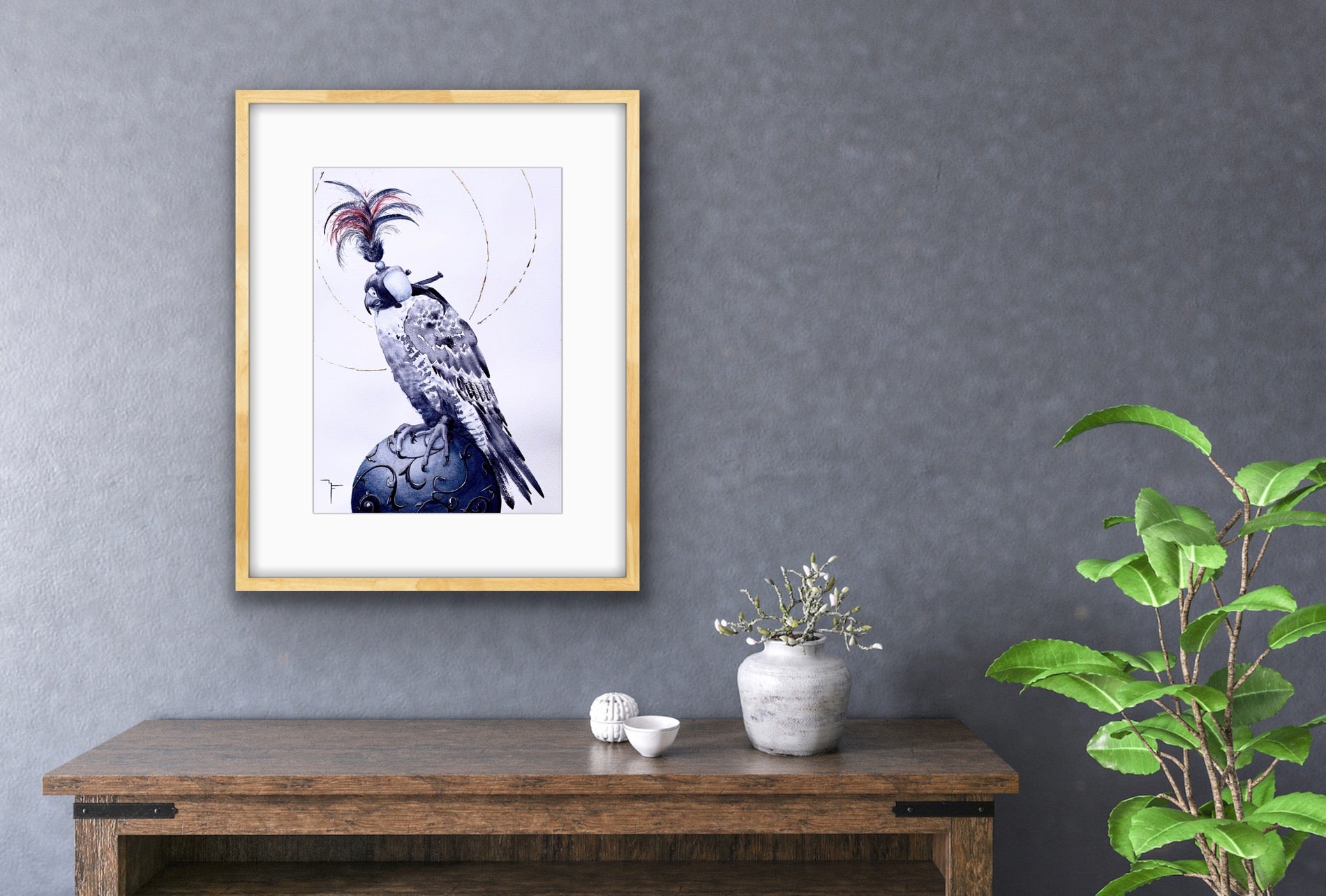 'Medieval Falcon' Peregrine Falcon fine art print by Marina Fox, framed in natural timber, displayed above a rustic oak console with a white ceramic vase and botanicals against a textured slate blue wall