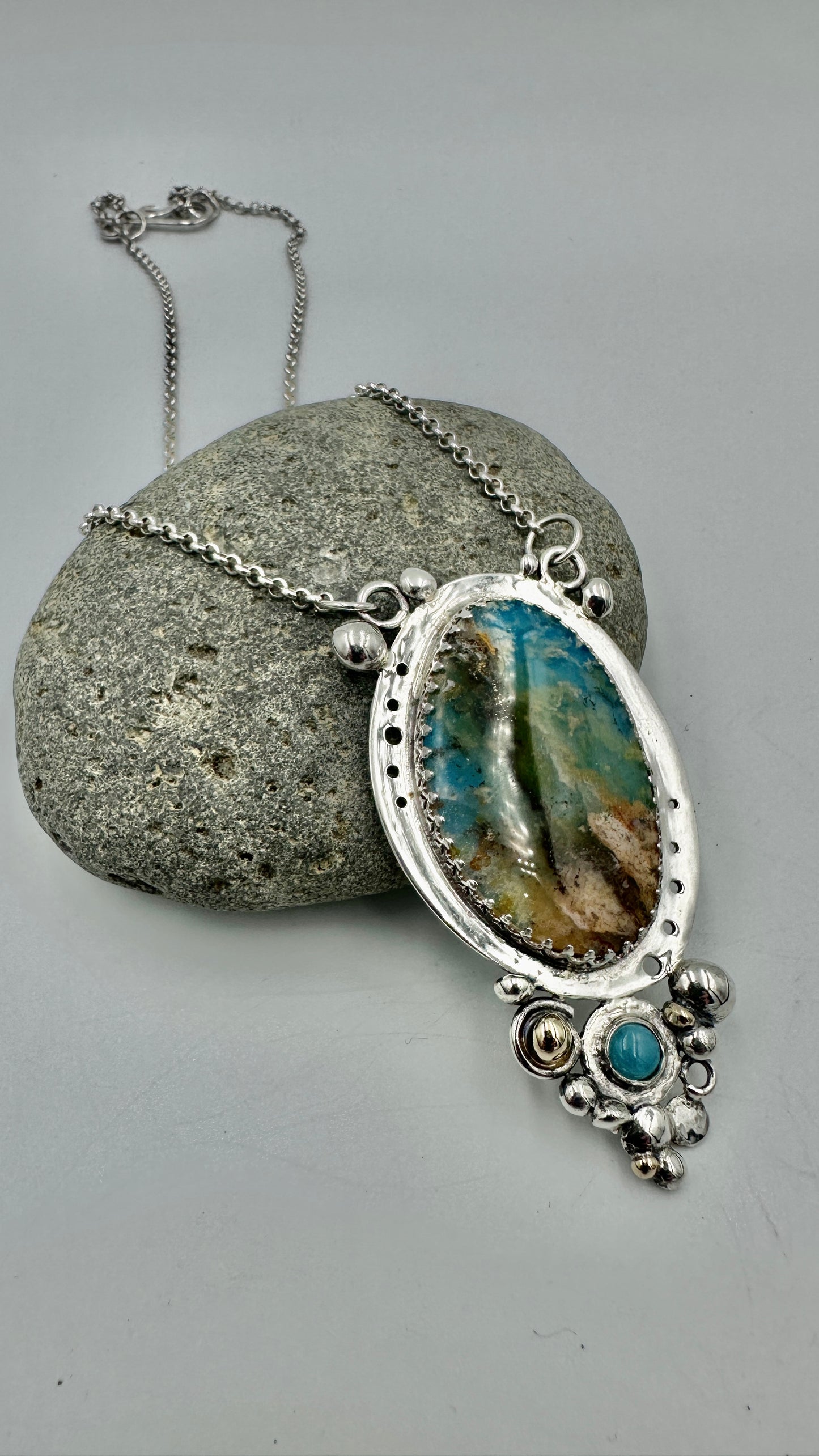 Silver Regency Plume Silver Bubble necklace with a pendant on a gray rock