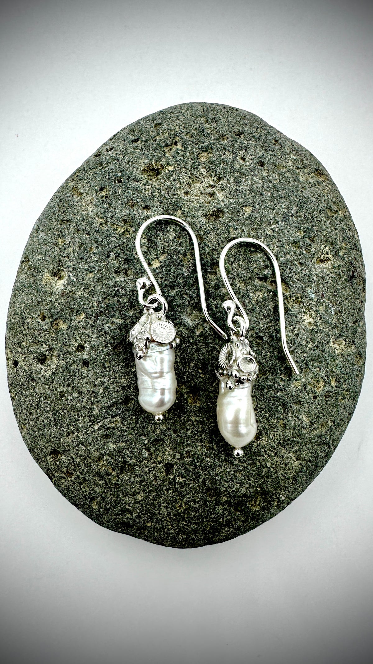 Pair of baroque freshwater pearl and sterling silver coral sea drop earrings laid flat on a smooth grey stone
