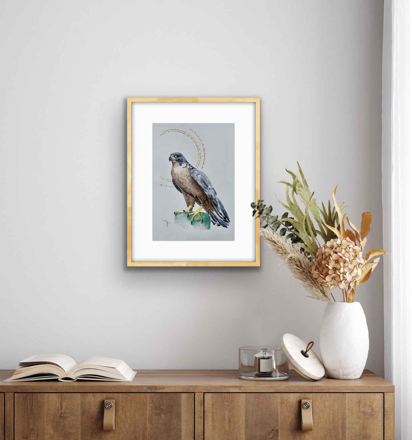 'Poise' Peregrine Falcon fine art print by Marina Fox, framed in natural timber, displayed above a warm oak sideboard with dried botanicals in a soft grey Scandinavian-style interior