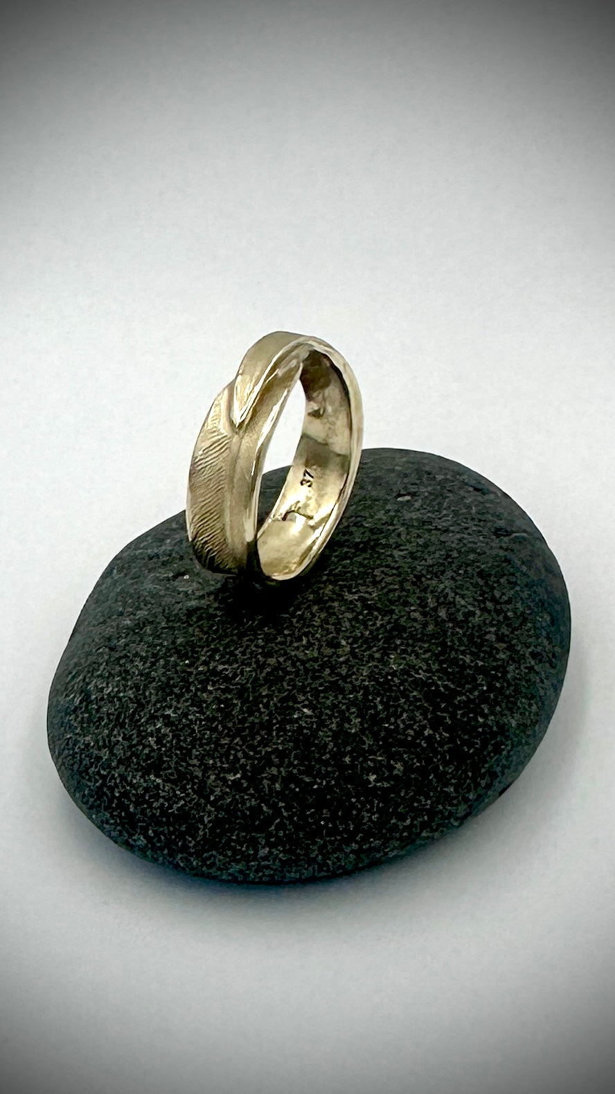 Side profile of 9 carat gold feather ring on dark stone, showing the flowing wrap of the band cast from a real feather — Marina Fox Fine Art