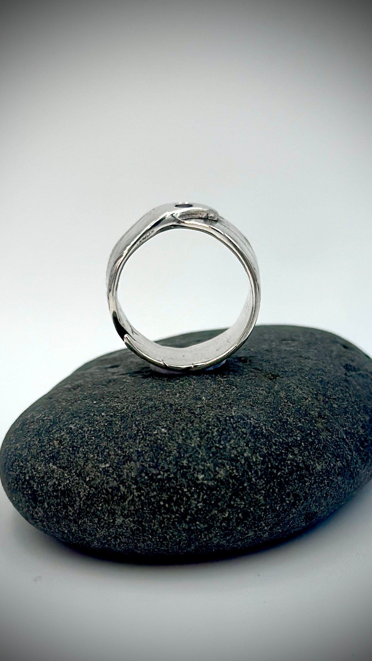 Side profile of sterling silver feather ring standing upright on dark river stone, showing open circular band form and smooth polished interior — Marina Fox Fine Art