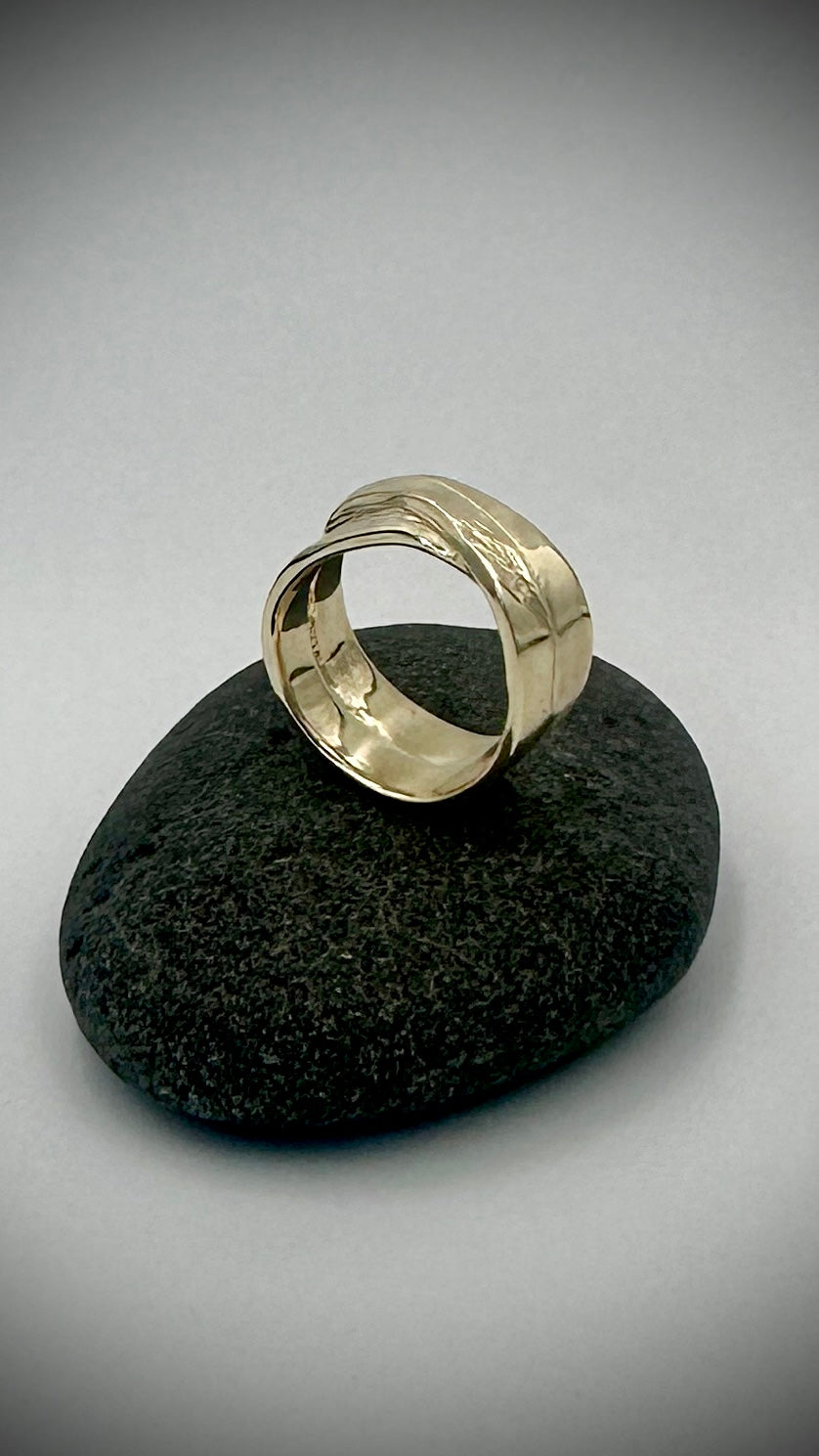 Side view of 9 carat yellow gold feather ring resting on dark river stone, showing smooth polished interior and wide band — Marina Fox Fine Art