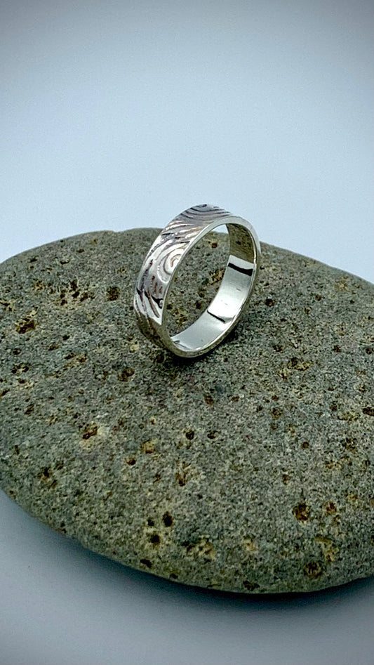 Side view of sterling silver Wave texture stacking ring on grey river stone
