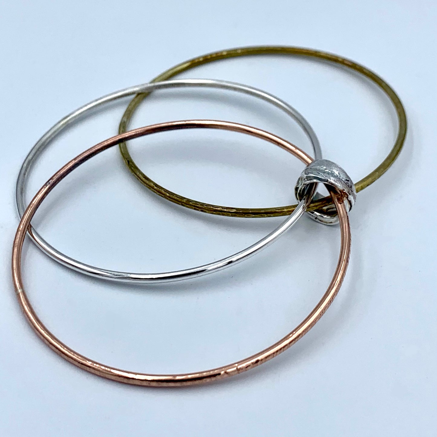 Side view of triple bangle set displaying unique handmade feather bead in solid sterling silver