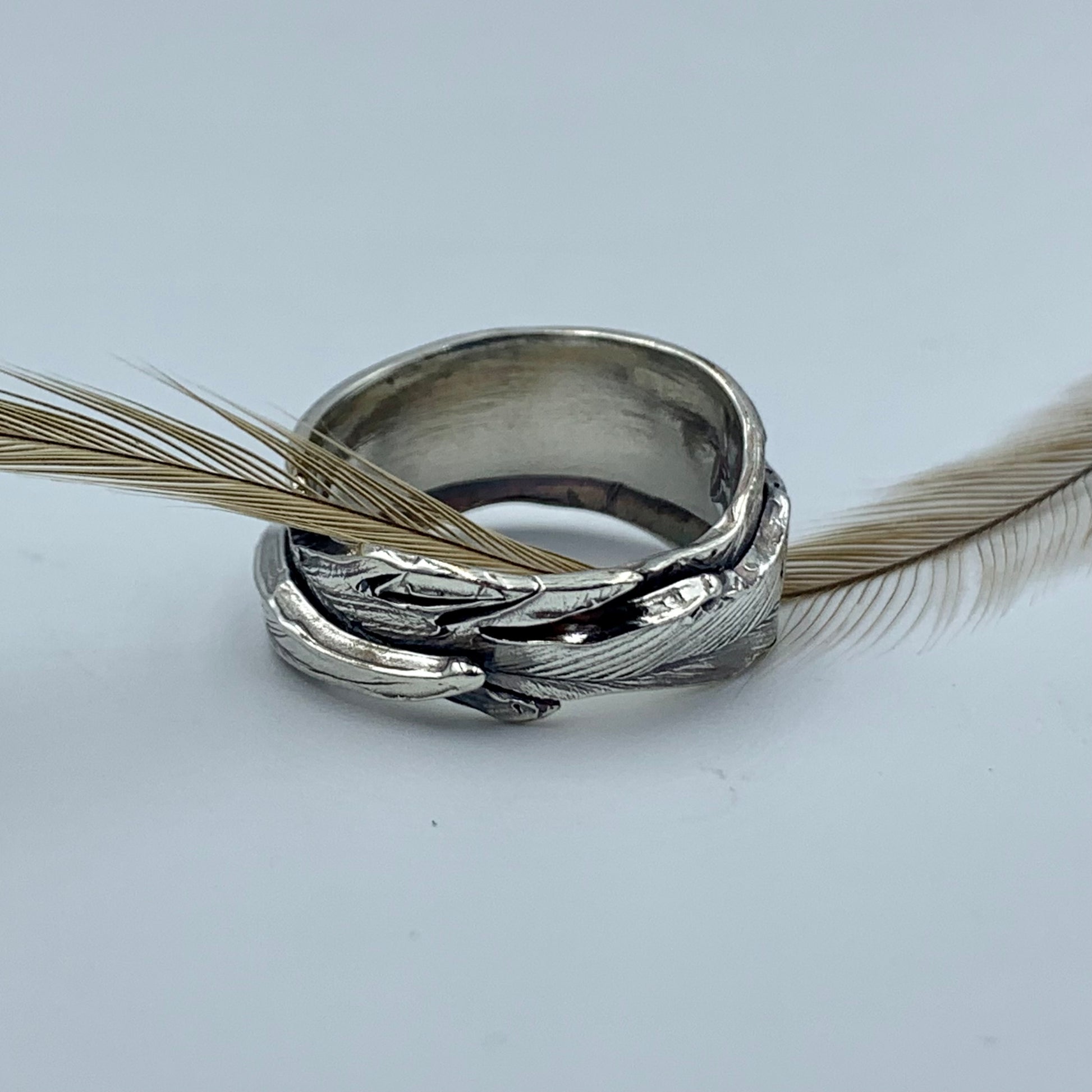 Sterling silver Australian emu feather ring displayed with a natural emu feather, showing full feather wrap texture and oxidised finish