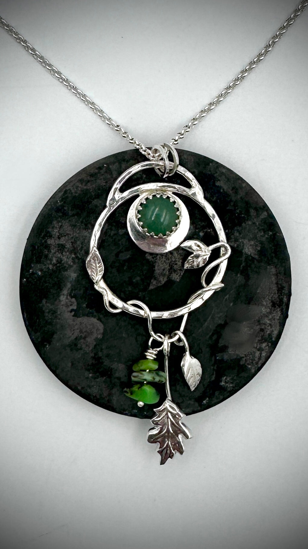Sterling silver Dryad pendant with green aventurine cabochon displayed against dark green stone disc, highlighting crescent moon and nature-inspired charm details