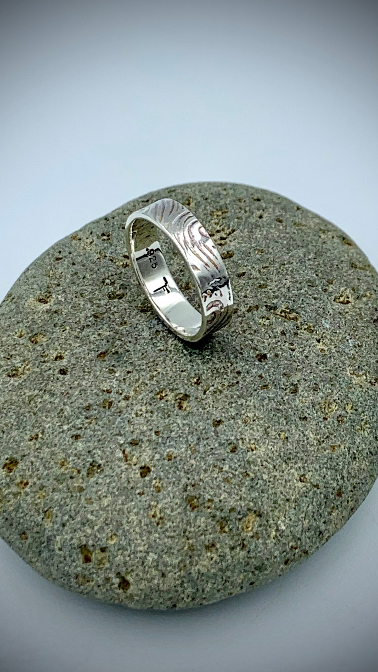 Sterling silver Wave textured ring draped over a natural river stone - nature-inspired fine art jewellery
