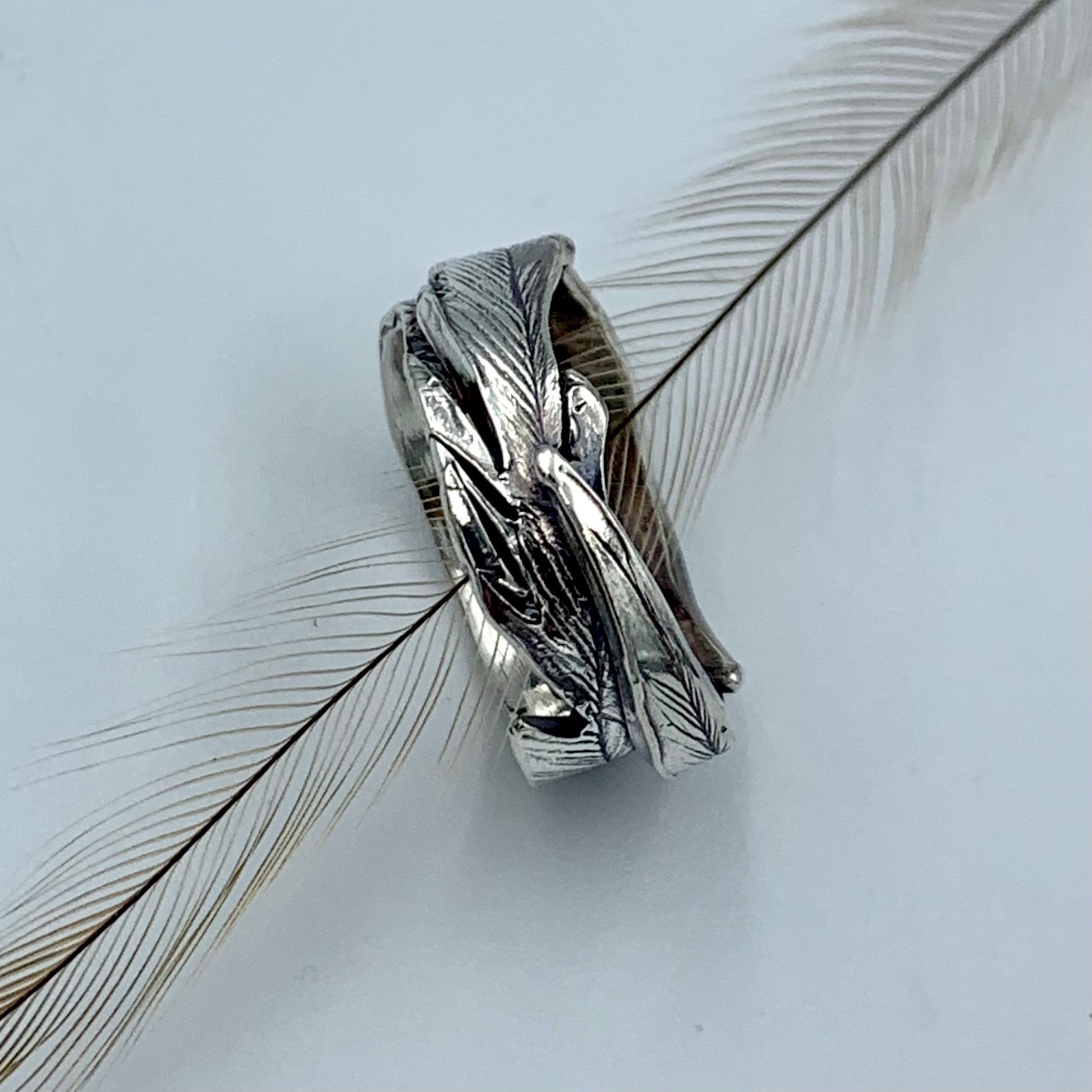 Sterling silver emu feather ring, side profile view with a natural emu feather threaded through the ring