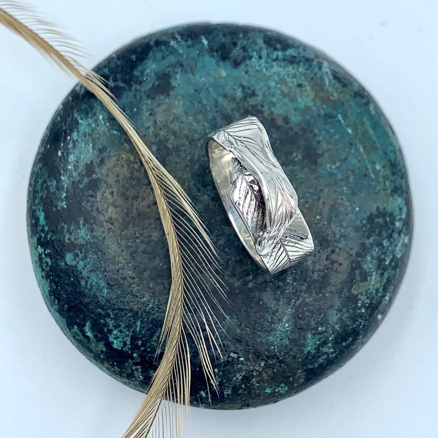 Sterling silver emu feather ring tilted to show smooth polished interior band and oxidised feather-imprinted exterior, displayed on a dark green stone with a natural emu feather