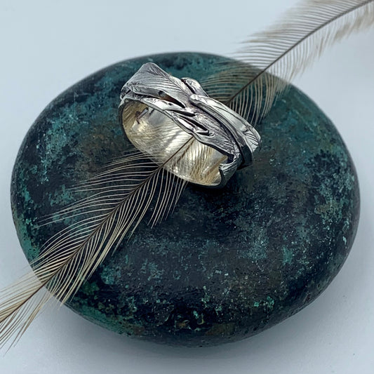 Sterling silver emu feather ring, top view showing layered feather texture with oxidised detailing, resting on a natural emu feather