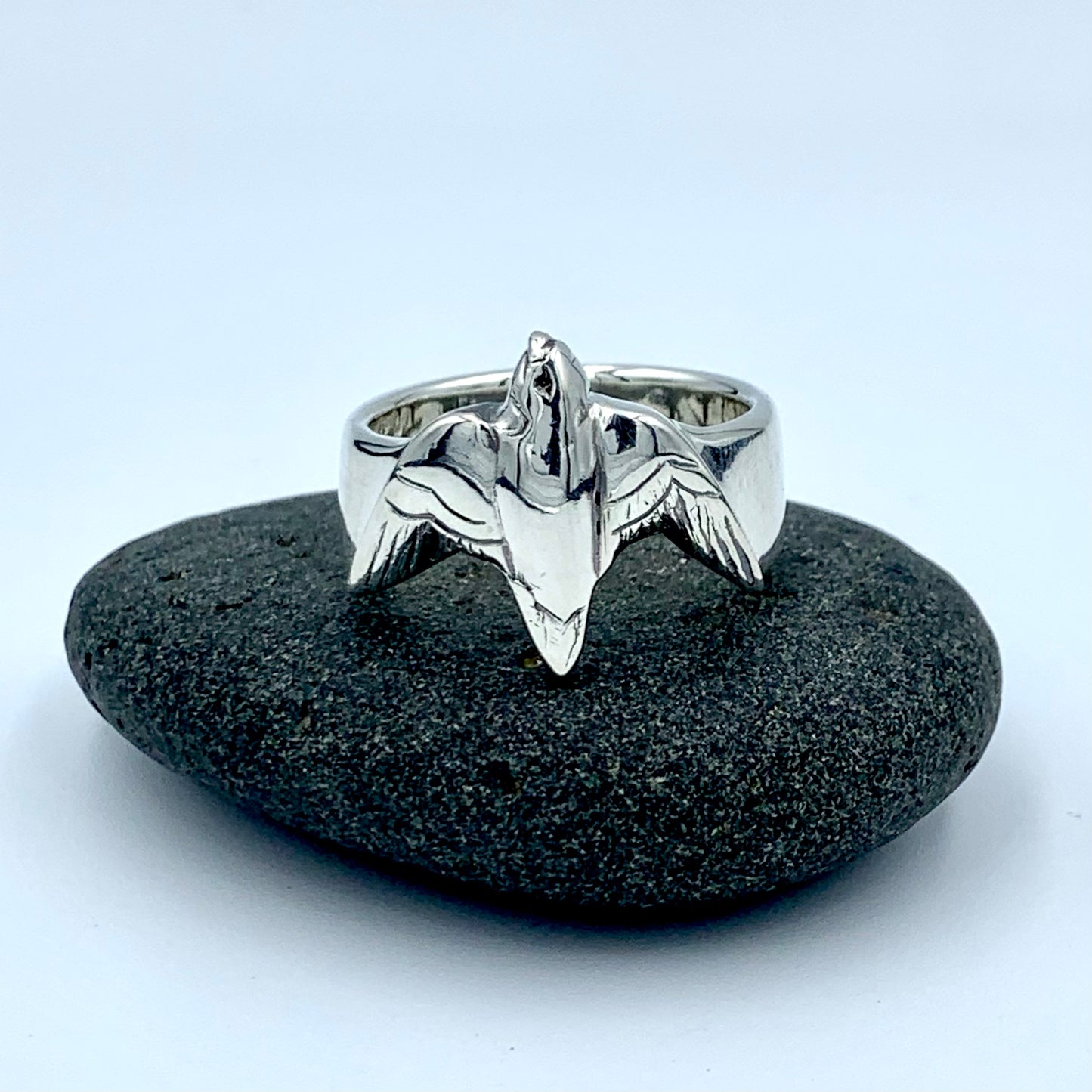 Sterling silver falconer's ring, front-facing view on a dark river stone, showing sculpted raptor in flight with outstretched wings and detailed feather engraving