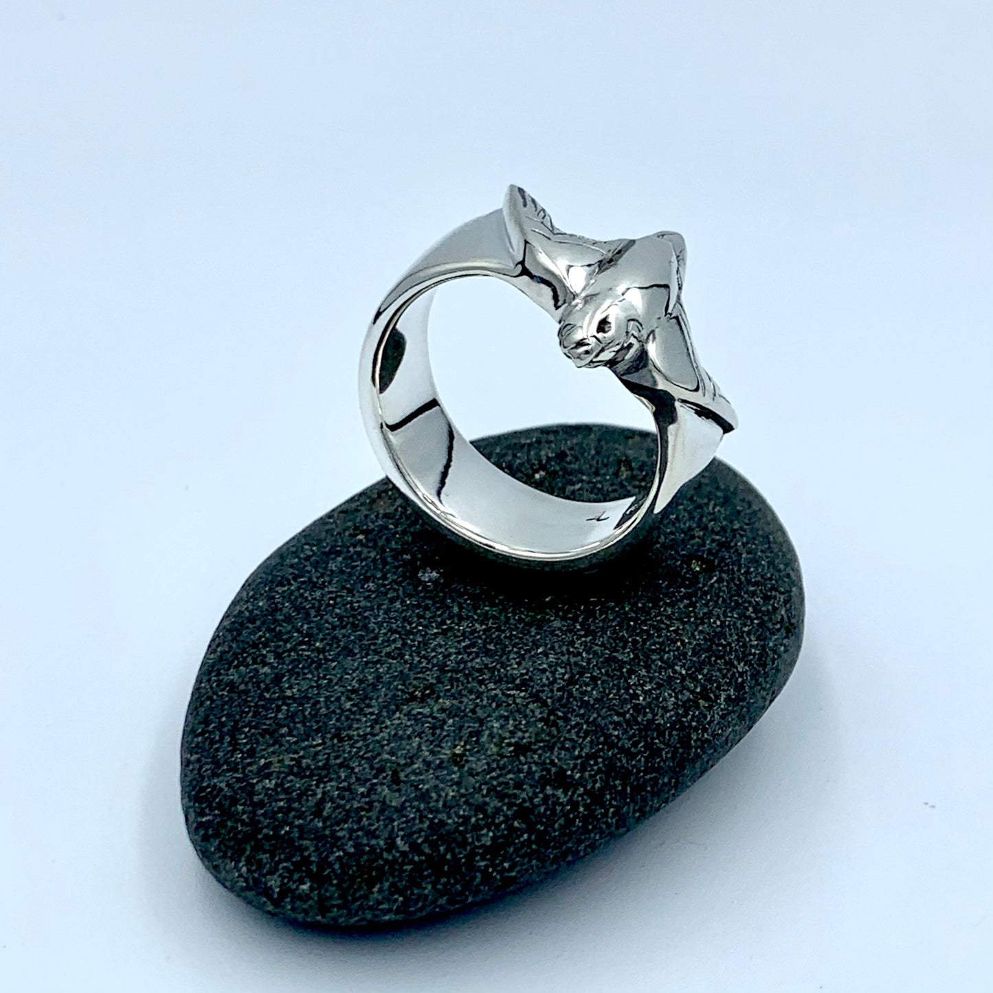 Sterling silver falconer's ring, side view on a dark river stone, showing polished wide interior band and sculpted bird figure wrapping around the shank