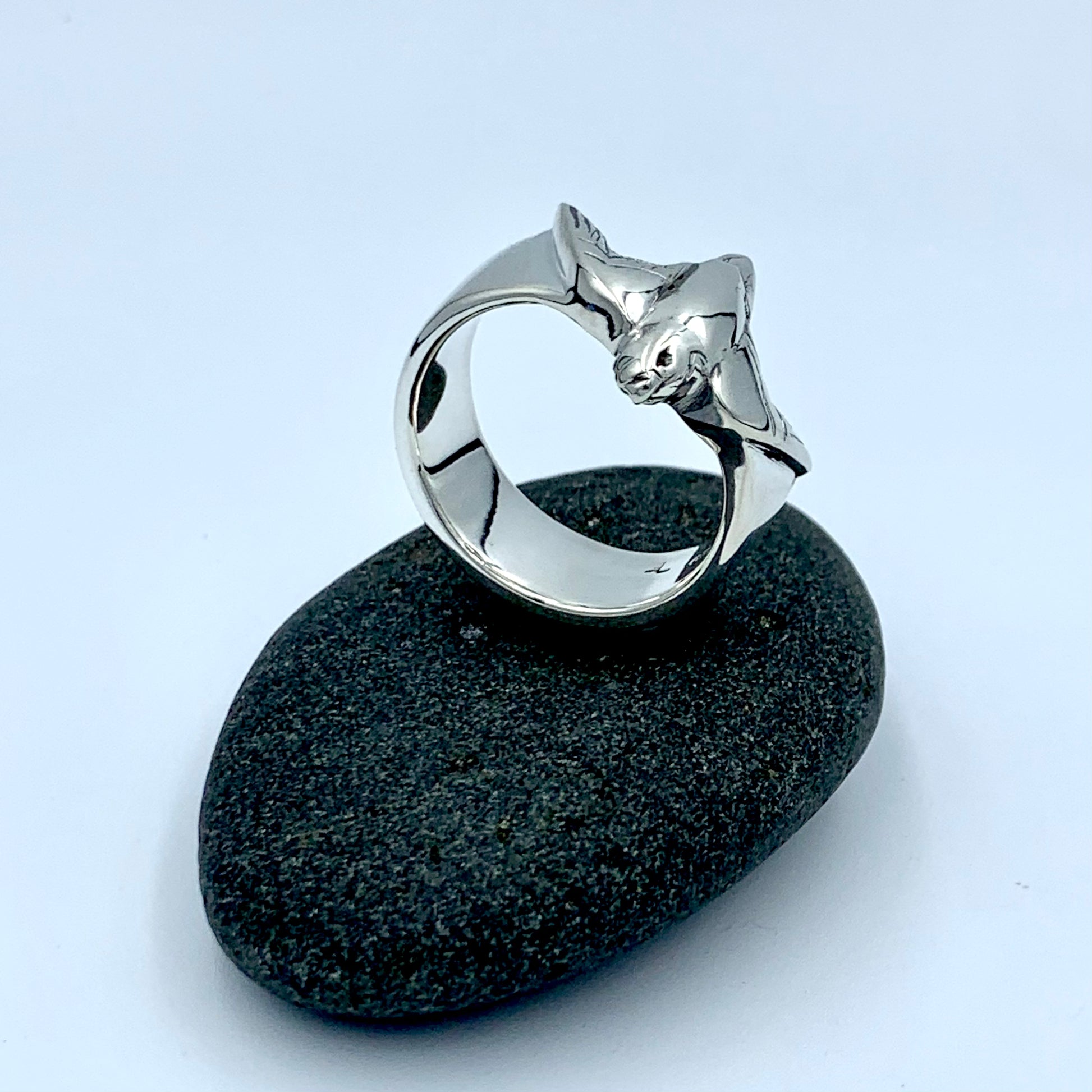 Sterling silver falconer's ring, side view on a dark river stone, showing polished wide interior band and sculpted bird figure wrapping around the shank