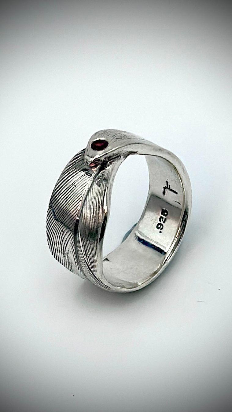 Sterling silver feather ring with red garnet gemstone set at the feather tip, angled view showing .925 hallmark inside band — Marina Fox Fine Art