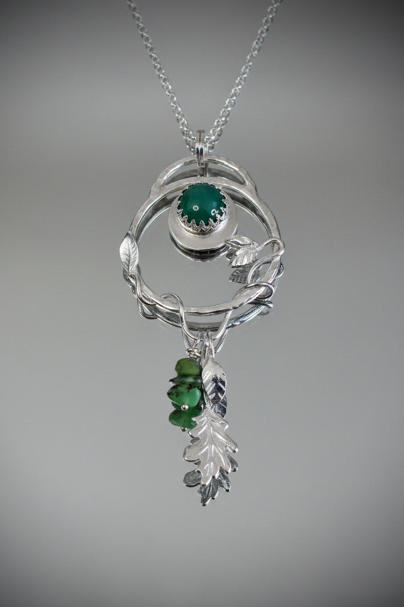 Sterling silver nature-inspired pendant necklace on a silver chain, front view featuring an organic twig-form circular frame with a bezel-set green adventurine cabochon, silver leaf details, and a drop of green gemstone chips and a sculpted silver oak leaf