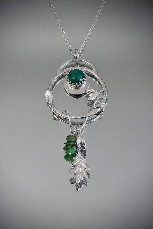Sterling silver nature-inspired pendant necklace on a silver chain, front view featuring an organic twig-form circular frame with a bezel-set green adventurine cabochon, silver leaf details, and a drop of green gemstone chips and a sculpted silver oak leaf