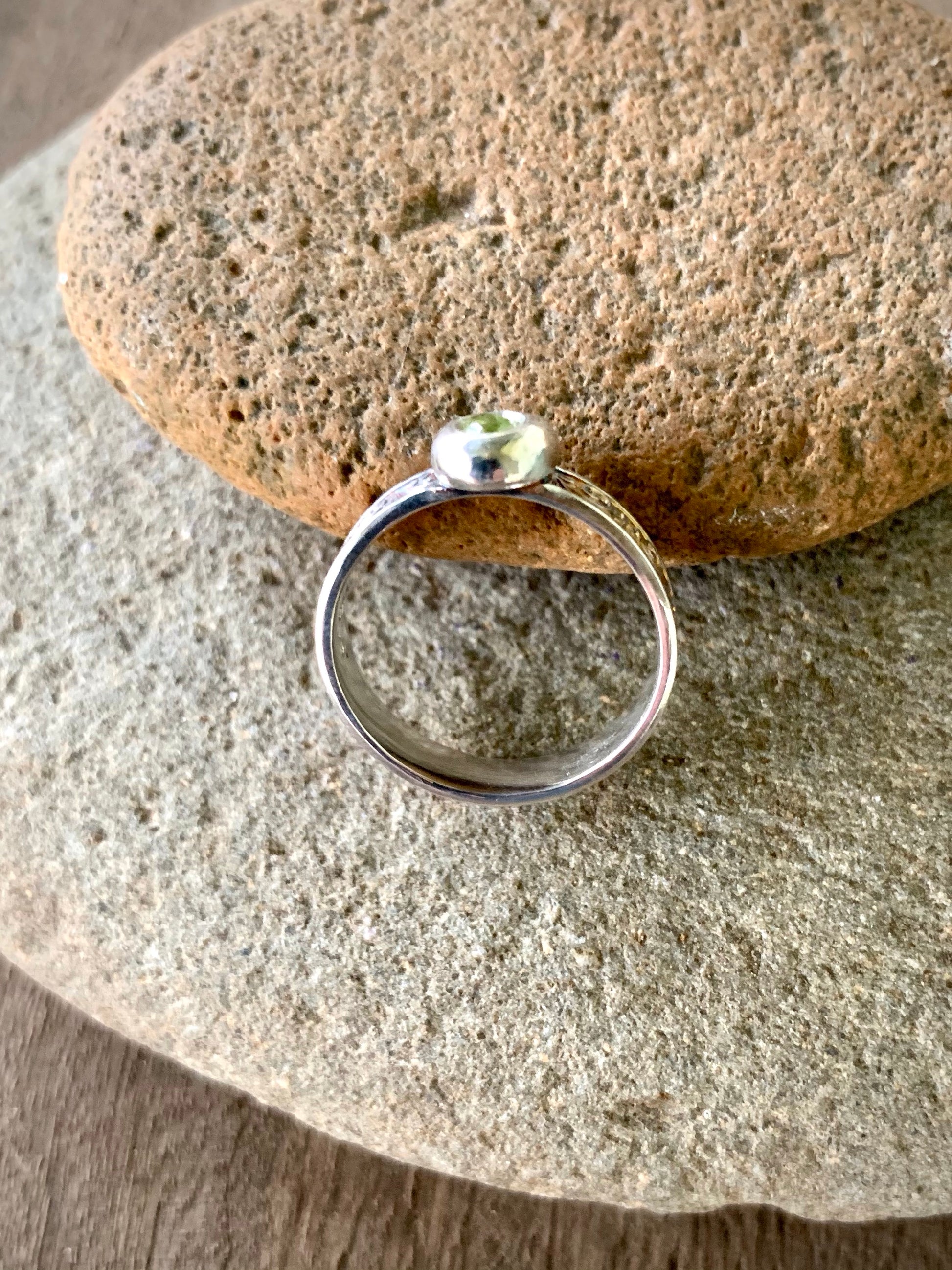 Sterling silver ring with round flush-set peridot and scroll engraved band on sandstone, warm natural light