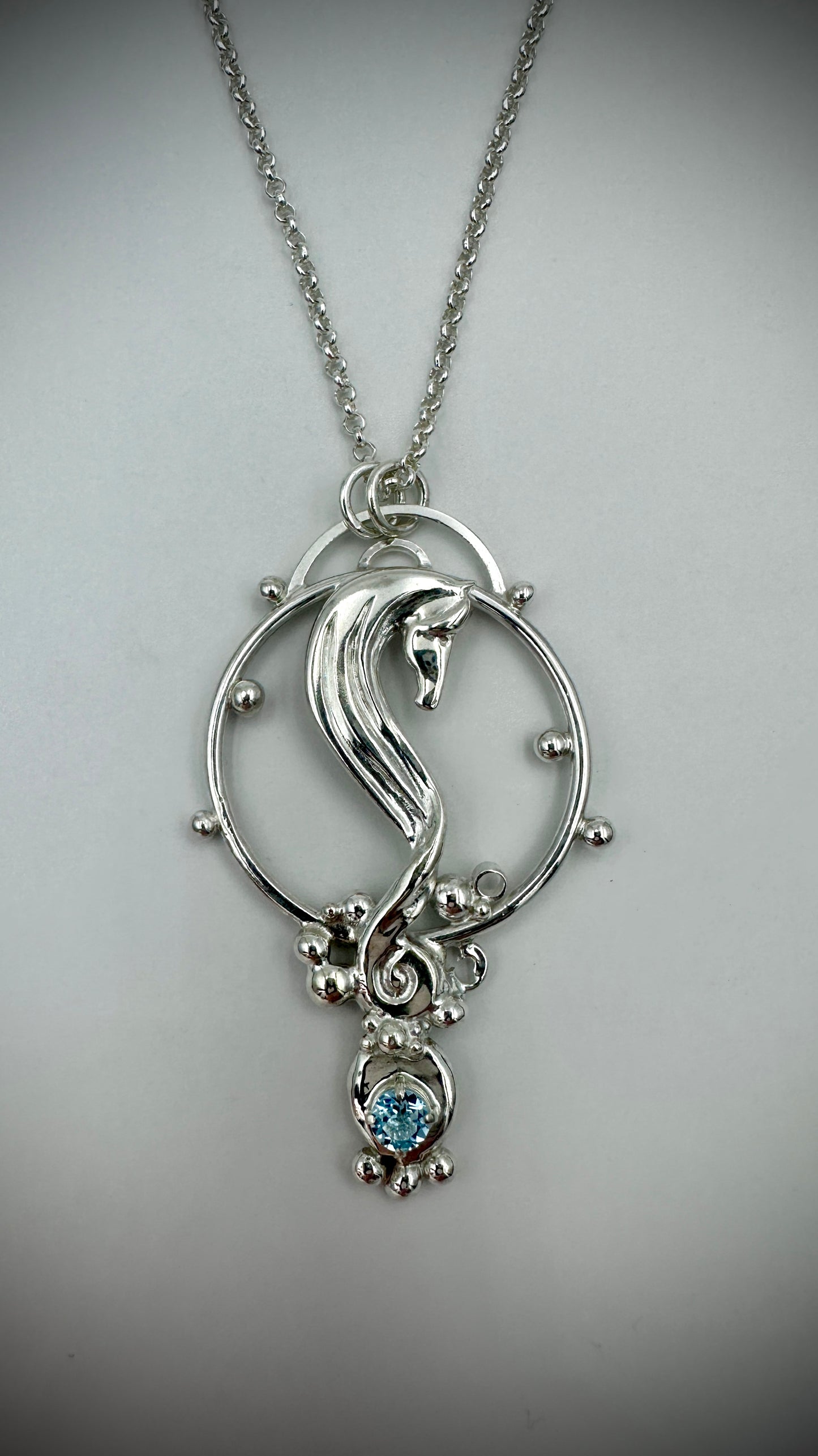 Sterling silver seahorse pendant on a belcher chain, displayed against a white background, with blue topaz drop and granulation detail around a circular frame