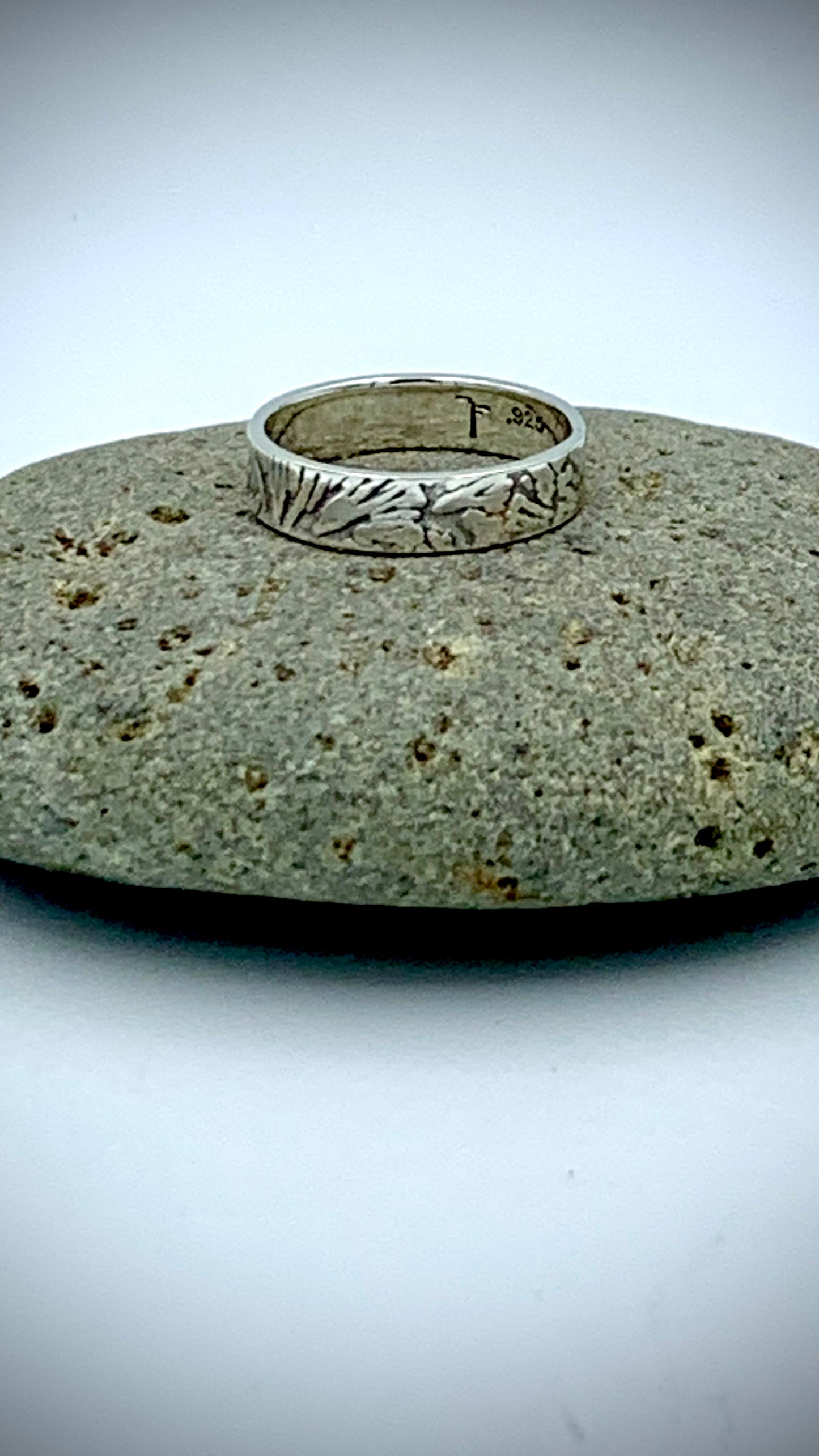 Sterling silver stacking ring with organic Ginkgo leaf  texture, resting on a smooth grey river stone