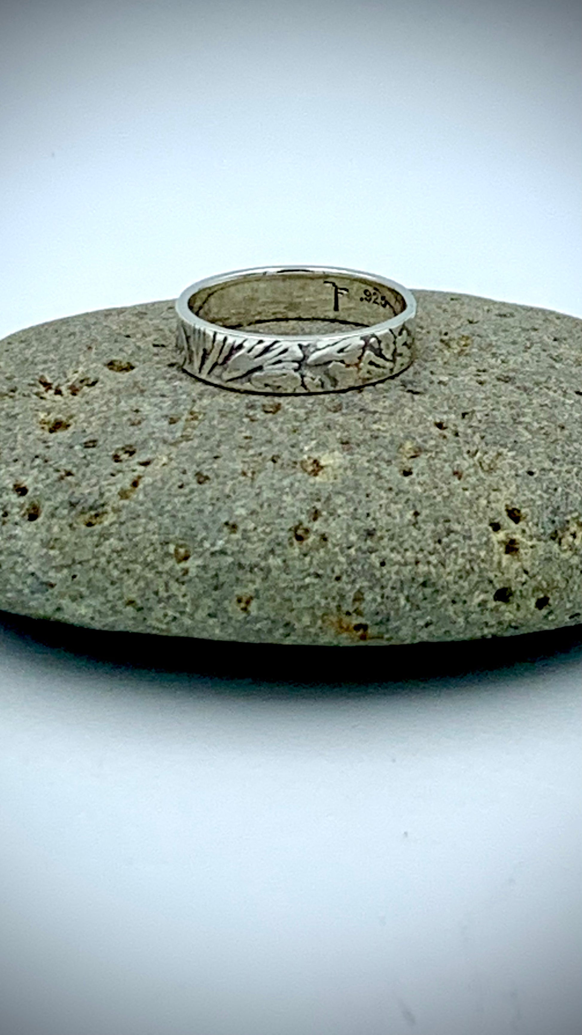 Sterling silver stacking ring with organic Ginkgo leaf  texture, resting on a smooth grey river stone