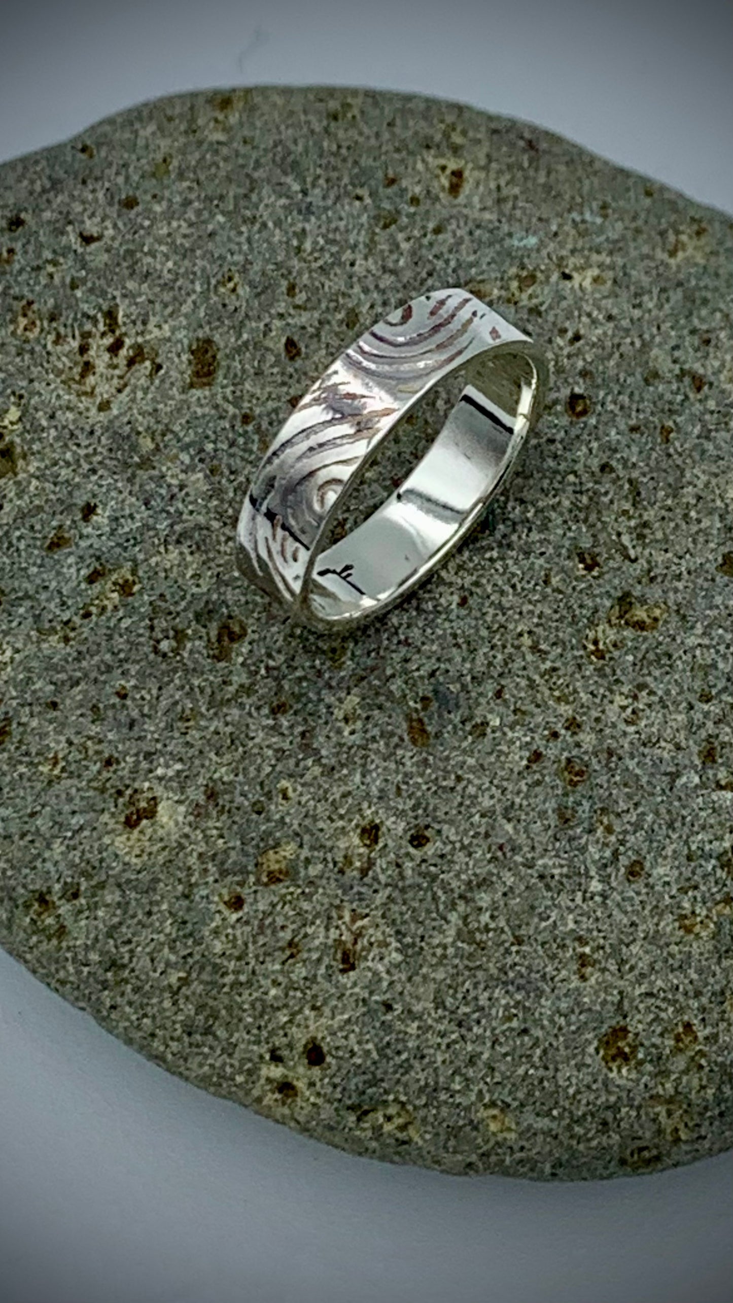 Sterling silver stacking ring with organic Wave texture, resting on a smooth grey river stone