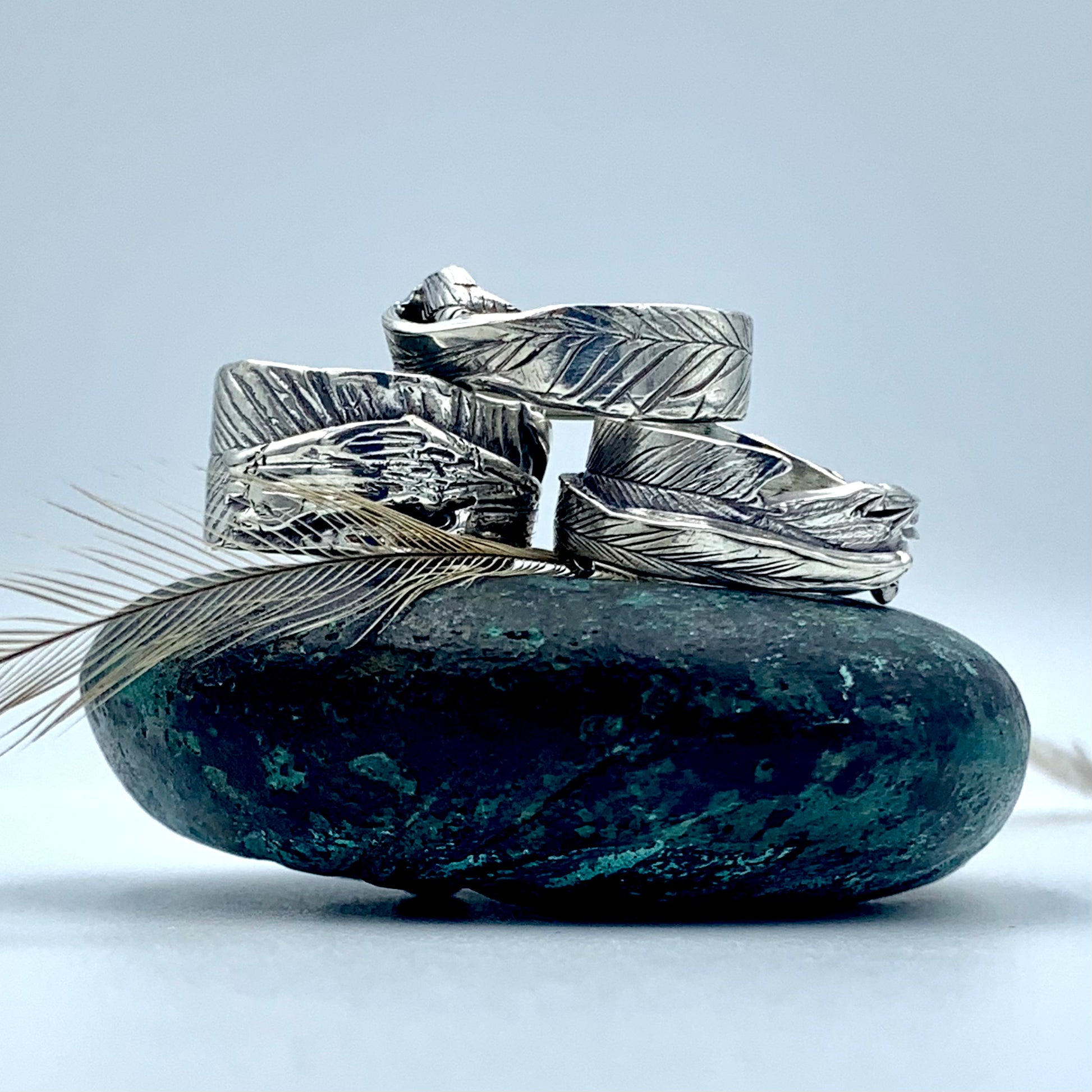 Three sterling silver emu feather imprinted rings alongside a natural emu feather, showing full wrap feather texture and oxidised details