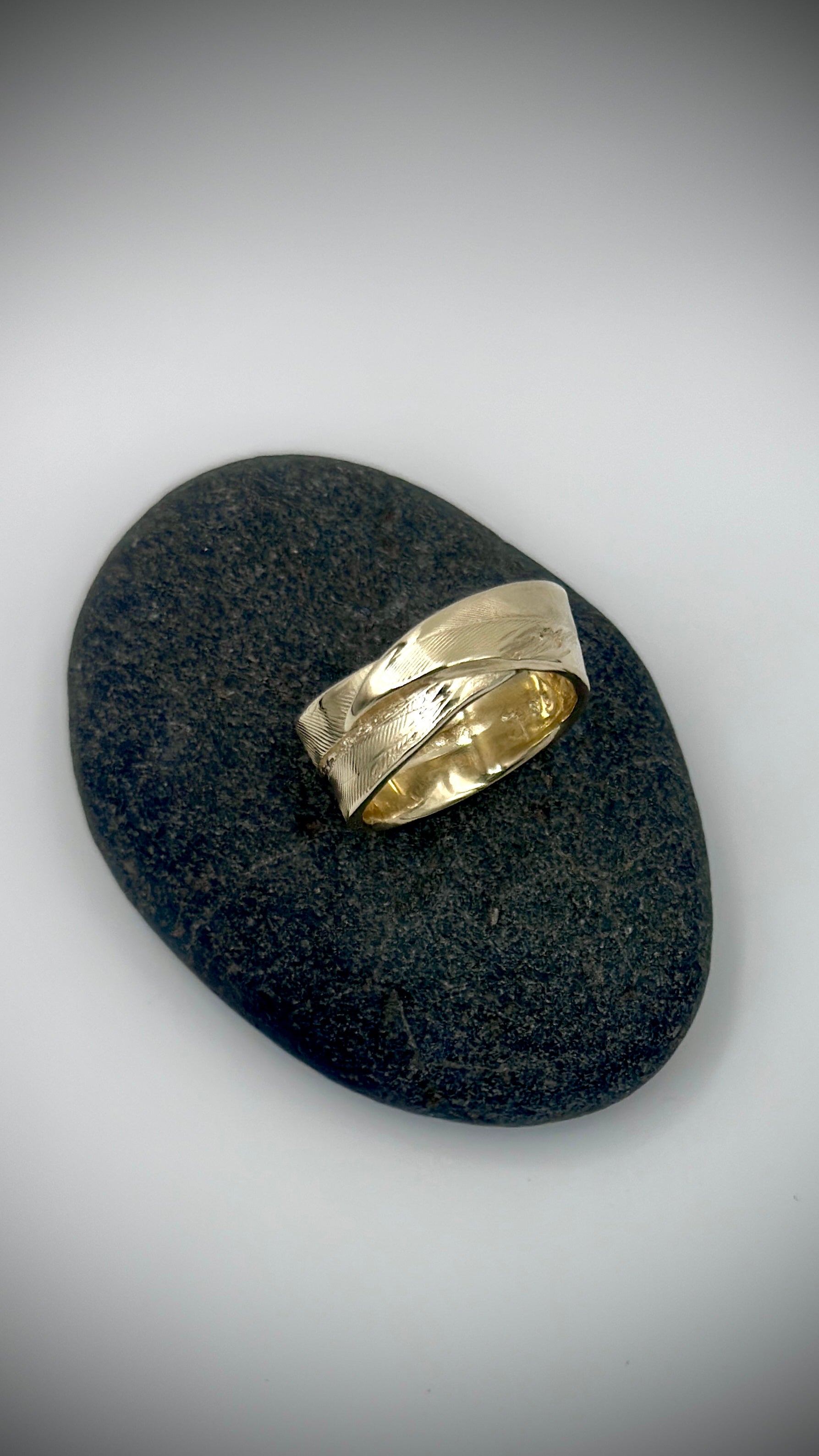 Top-down view of 9 carat yellow gold feather ring lying on dark river stone, revealing full lost wax cast feather surface — Marina Fox Fine Art