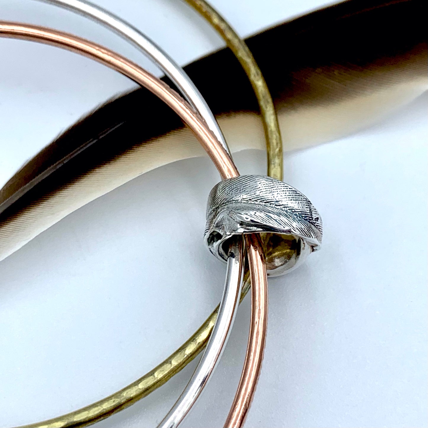 Triple bangle set featuring sterling silver, brass and copper bangles linked through a cast sterling silver feather bead 